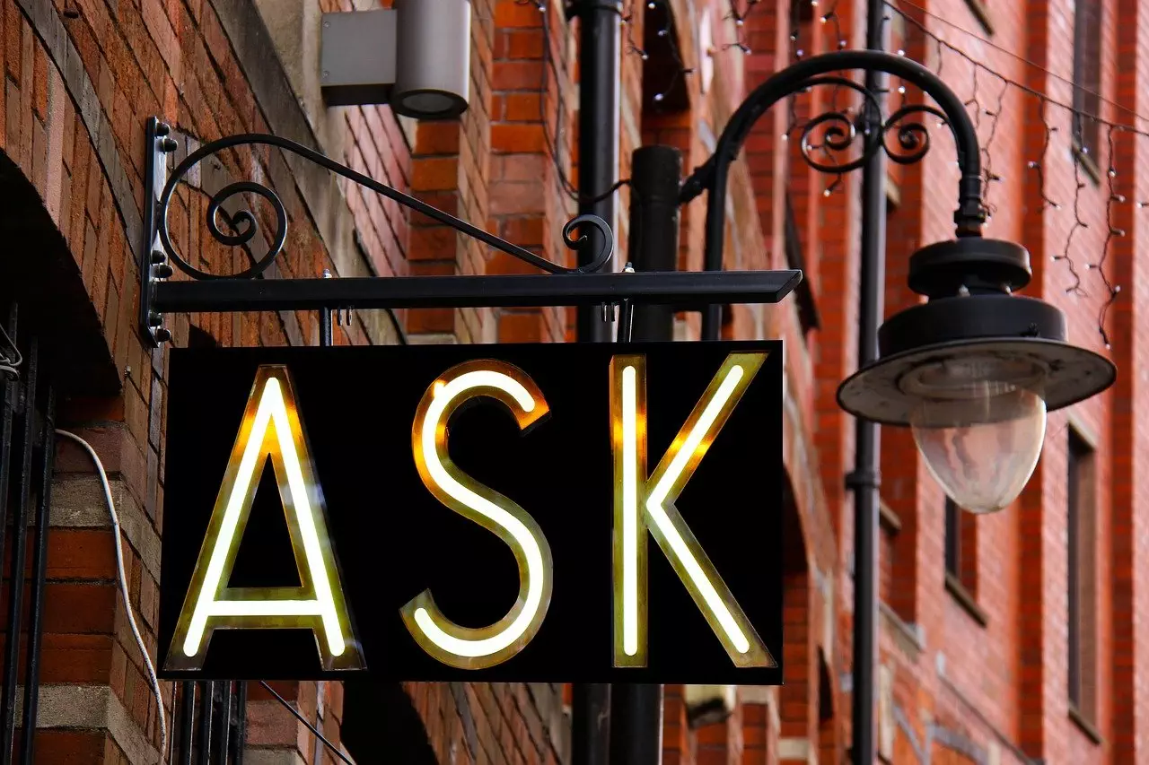 Storefront sign that says "ASK" in front of lamp and red building walls