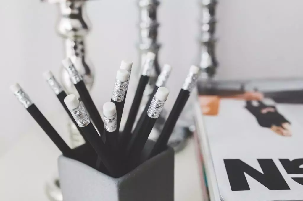 Close up shot of multiple black pencils in a cup with a notebook in the background
